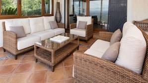 A cozy living area with wicker furniture, a glass coffee table, and large windows offering a view of the outdoors. - Centauro by Interhome (Jávea)
