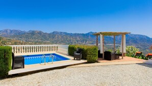 A pool area with a pergola and seating, surrounded by a white fence, with mountains in the background. - Villa Montemar by Interhome (Nerja)