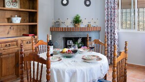 A dining area with a round table set for four, surrounded by wooden chairs. A fireplace with decorative tiles and a potted plant is visible in the background. - Villa Montemar by Interhome (Nerja)