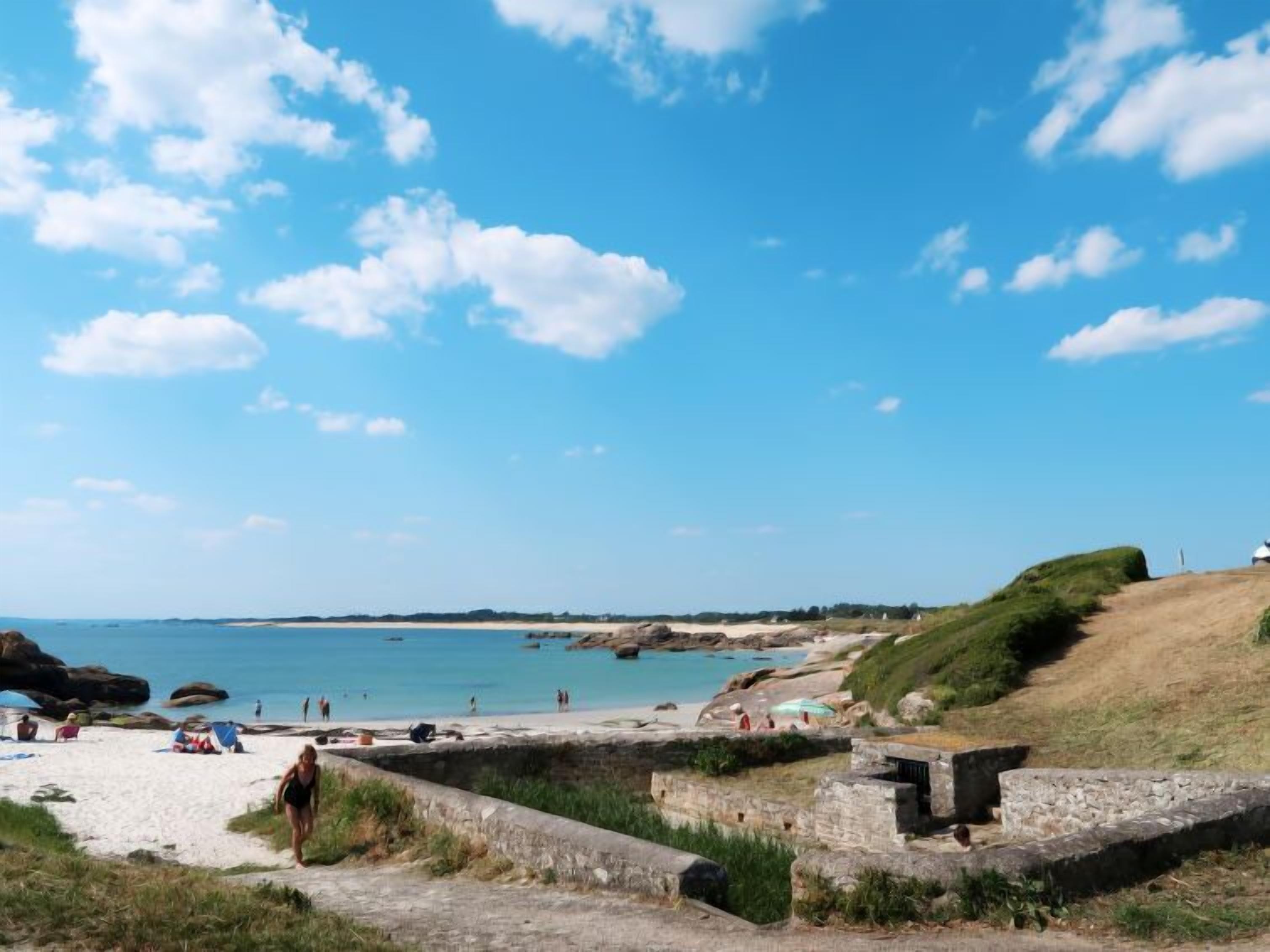 A beach with clear skies, a sandy shore, and a stone wall.