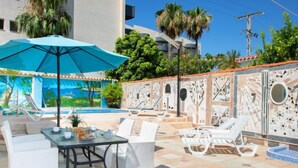 A poolside area with lounge chairs, a table with chairs, and a blue umbrella. - Vacation home Pedro by Interhome (Albir)
