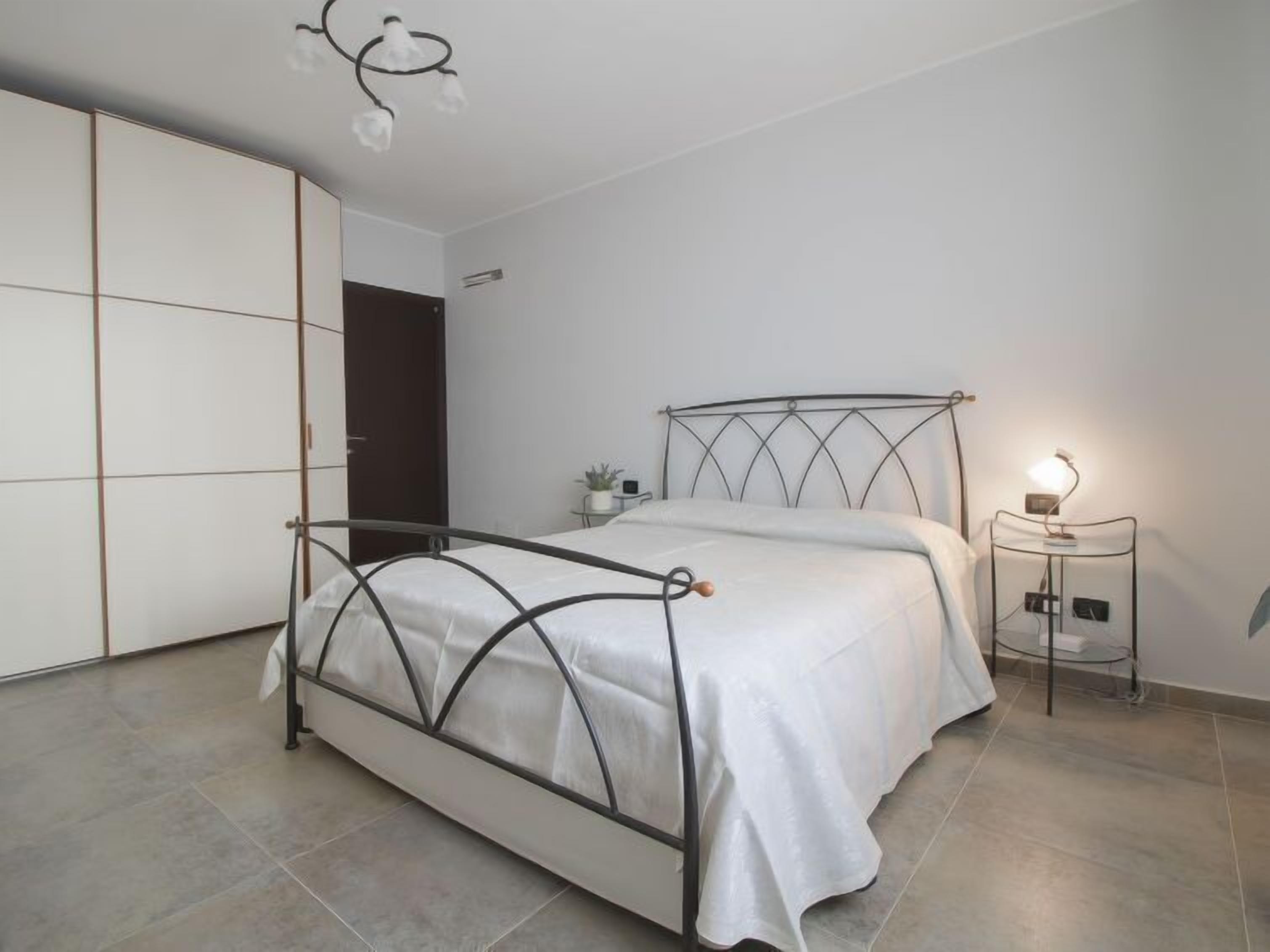 A modern bedroom with a metal bed frame, a bedside table with a lamp, and a wardrobe with sliding doors.