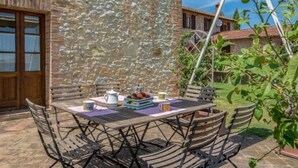 Un patio al aire libre con un muro de piedra, una mesa de madera con sillas y una planta en maceta.