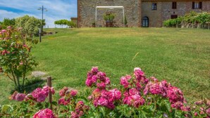 Un edificio de piedra con una entrada central, rodeado de un césped y plantas florecientes.