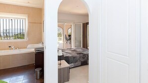 Un baño moderno con bañera, lavamanos e inodoro. Hay una ventana con barrotes y vistas al exterior.