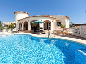 A swimming pool with lounge chairs and umbrellas, a building with arches and a tiled roof, and a clear blue sky. - Vacation home Capi by Interhome (Pego)