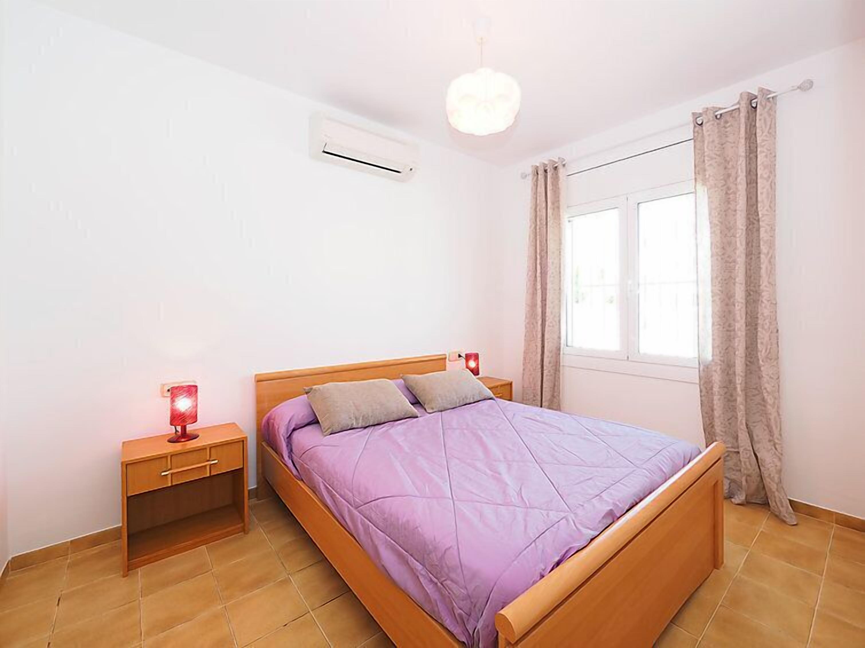 A bedroom with a wooden bed, a nightstand, a red lamp, and a window with curtains.