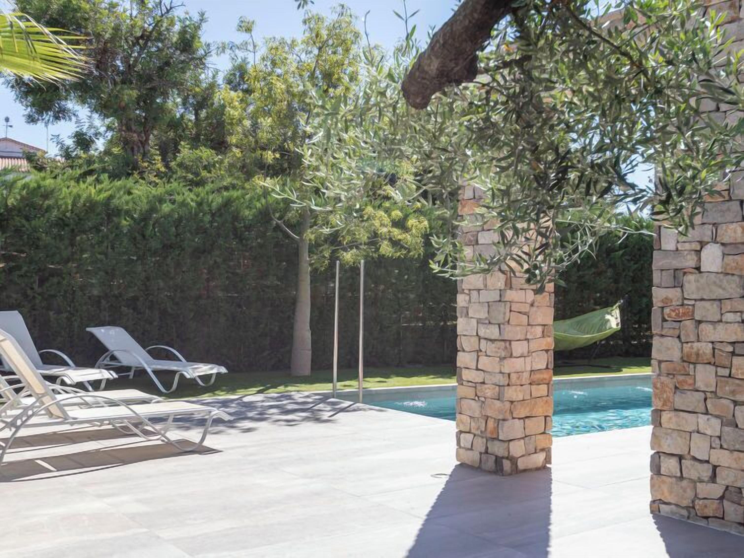 Un área de piscina al aire libre con pilares de piedra, sillones de descanso y una hamaca.