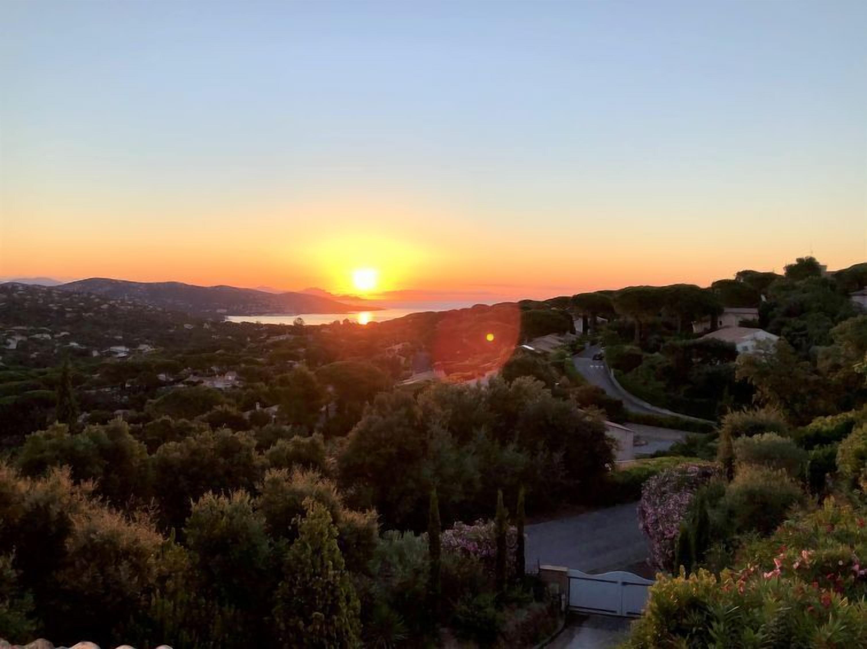 Vista do pôr do sol sobre uma paisagem costeira, com uma estrada sinuosa e vegetação densa.