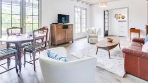 A spacious living room with a wooden dining table, chairs, a sofa, and a television on a wooden cabinet. - Mauriac by Interhome (Capbreton)