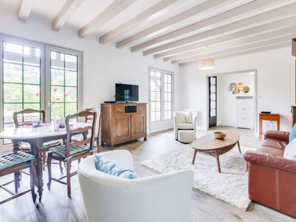 A spacious living room with a wooden dining table, chairs, a sofa, and a television on a wooden cabinet.