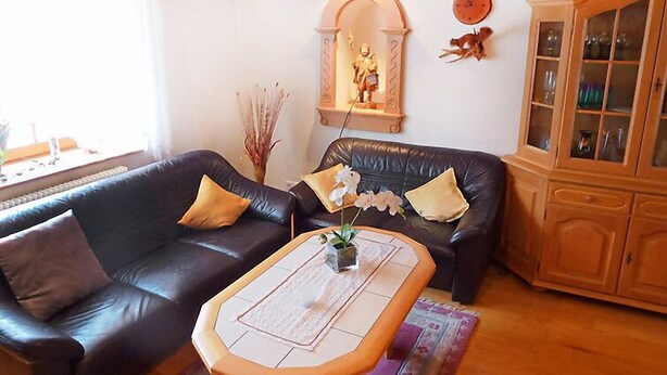 Una sala de estar con un sofá de cuero negro, una mesa de centro de madera y un mueble bar con puertas de cristal.