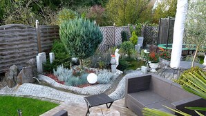 Un'area patio con arredi da esterno, un vialetto in pietra e un giardino con piante varie e un piccolo stagno.