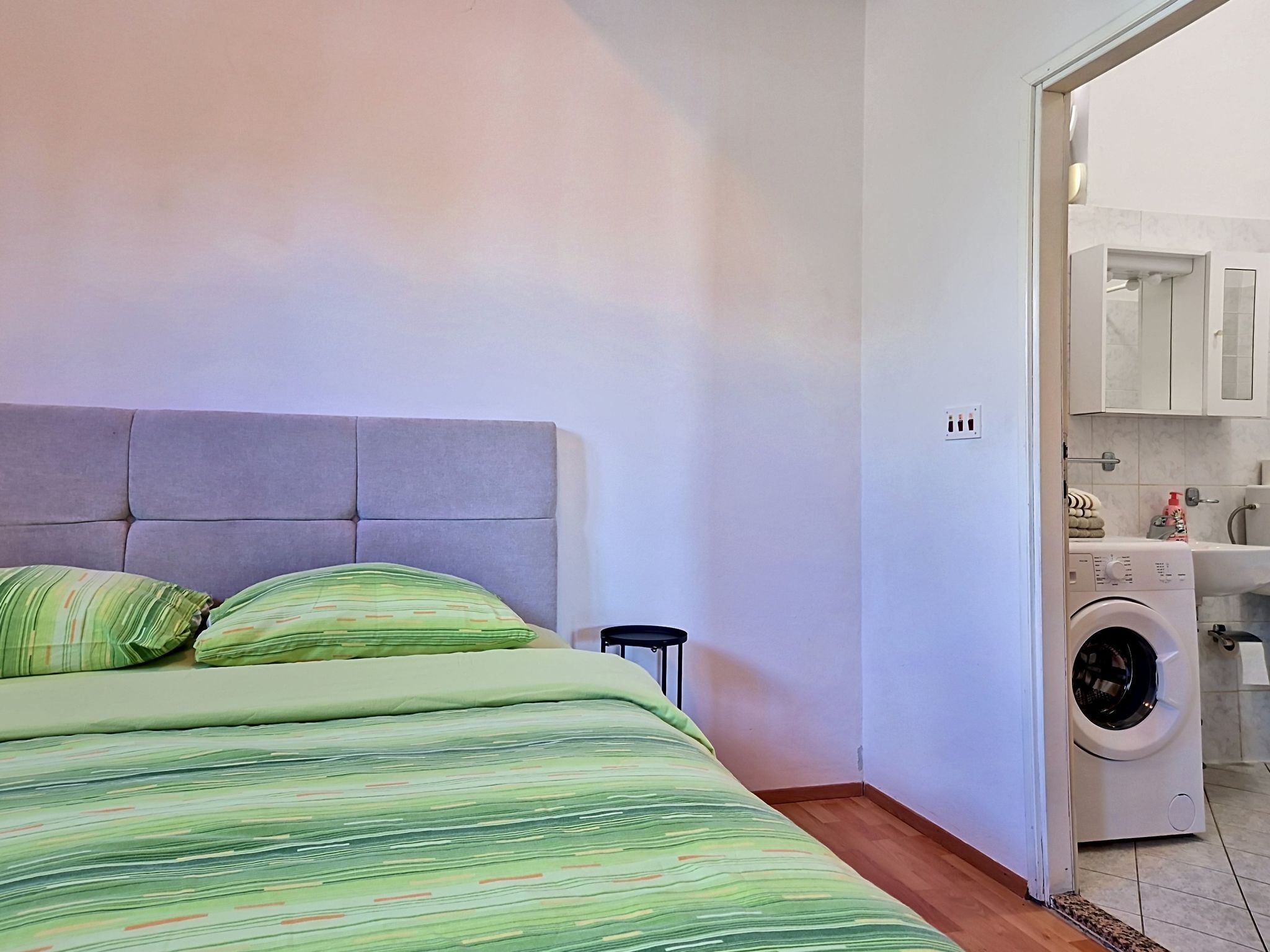 Une chambre à coucher avec un lit, un lave-linge et une salle de bain visible à travers une porte ouverte.