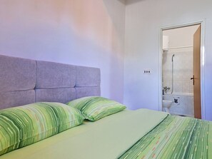 Ein Schlafzimmer mit Bett, Kissen, Kopfteil sowie ein Badezimmer mit Dusche und Toilette.