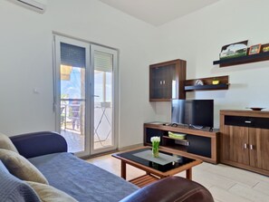 Een woonkamer met een bank, een salontafel, een televisie, houten kasten en een schuifdeur naar een buitenruimte.