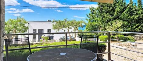 An outdoor patio with a round metal table and chairs, a beige canopy, and a view of a building and trees.