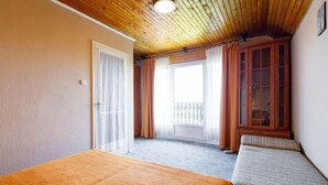 A room with a wooden ceiling, a bed with an orange bedspread, a window with curtains, and a wooden cabinet.