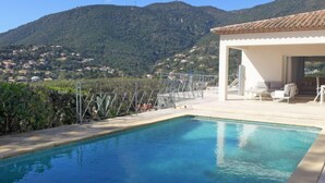 Una piscina con vista su una montagna e un edificio bianco con posti a sedere all'aperto.