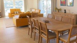 Un'ampia zona giorno con divano giallo, tavolo da pranzo in legno con sedie e una grande finestra vista all'esterno.
