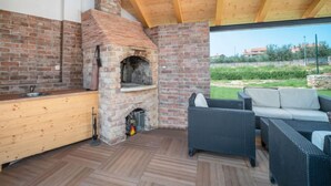 An outdoor kitchen area with a brick oven, wooden counter, and wicker furniture. - Apartment Ulika by Interhome (Poreč/Tar)