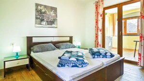 A double bed with a wooden headboard, two bedside tables with lamps, a painting above the bed, and a view of the outside through a door. - Apartment Ulika by Interhome (Poreč/Tar)