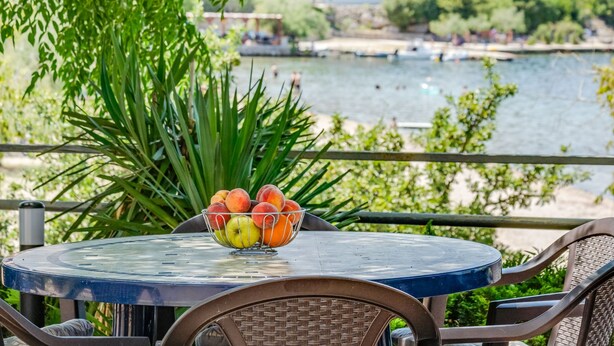 Ein Tisch mit Obstschale, mit Blick auf ein Gewässer und Gebäude im Hintergrund.
