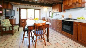 A cozy kitchen with wooden cabinets, a dining table with chairs, a television, and a tiled floor.