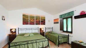 A bedroom with two beds, a window with curtains, and a wall with three paintings.