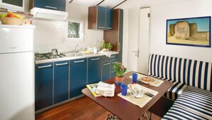 A compact kitchen with blue cabinets, a dining area with striped cushions, and a painting on the wall. - Cecina Mare by Interhome (Cecina)