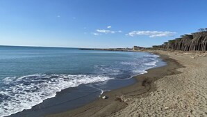 A beach with clear blue water, sandy shore, and a distant rocky outcrop. - Cecina Mare by Interhome (Cecina)