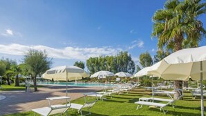 A poolside area with white lounge chairs and umbrellas, a clear blue sky, and palm trees. - Cecina Mare by Interhome (Cecina)