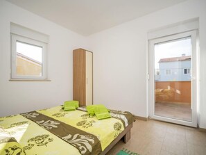 Ein Schlafzimmer mit einem Bett, einem Holzschrank, einer Glastür zum Balkon und einem Fenster.