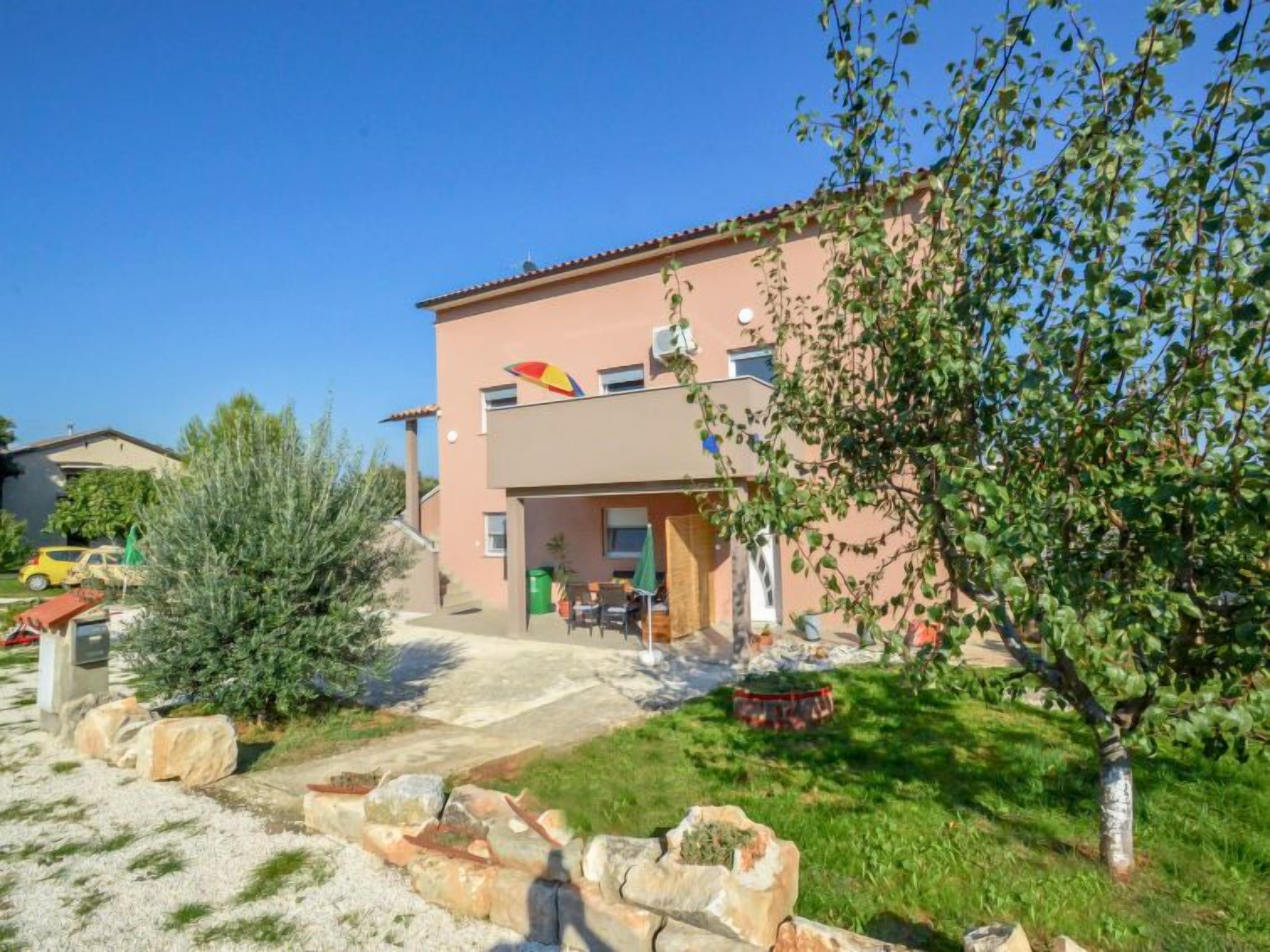 A two-story building with a flat roof, a small patio area with outdoor furniture, and a garden with rocks and shrubs.