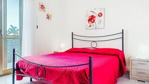 A bedroom with a metal bed frame, a red bedspread, and two wall-mounted lamps. - Apartment Clara by Interhome (Mascali)