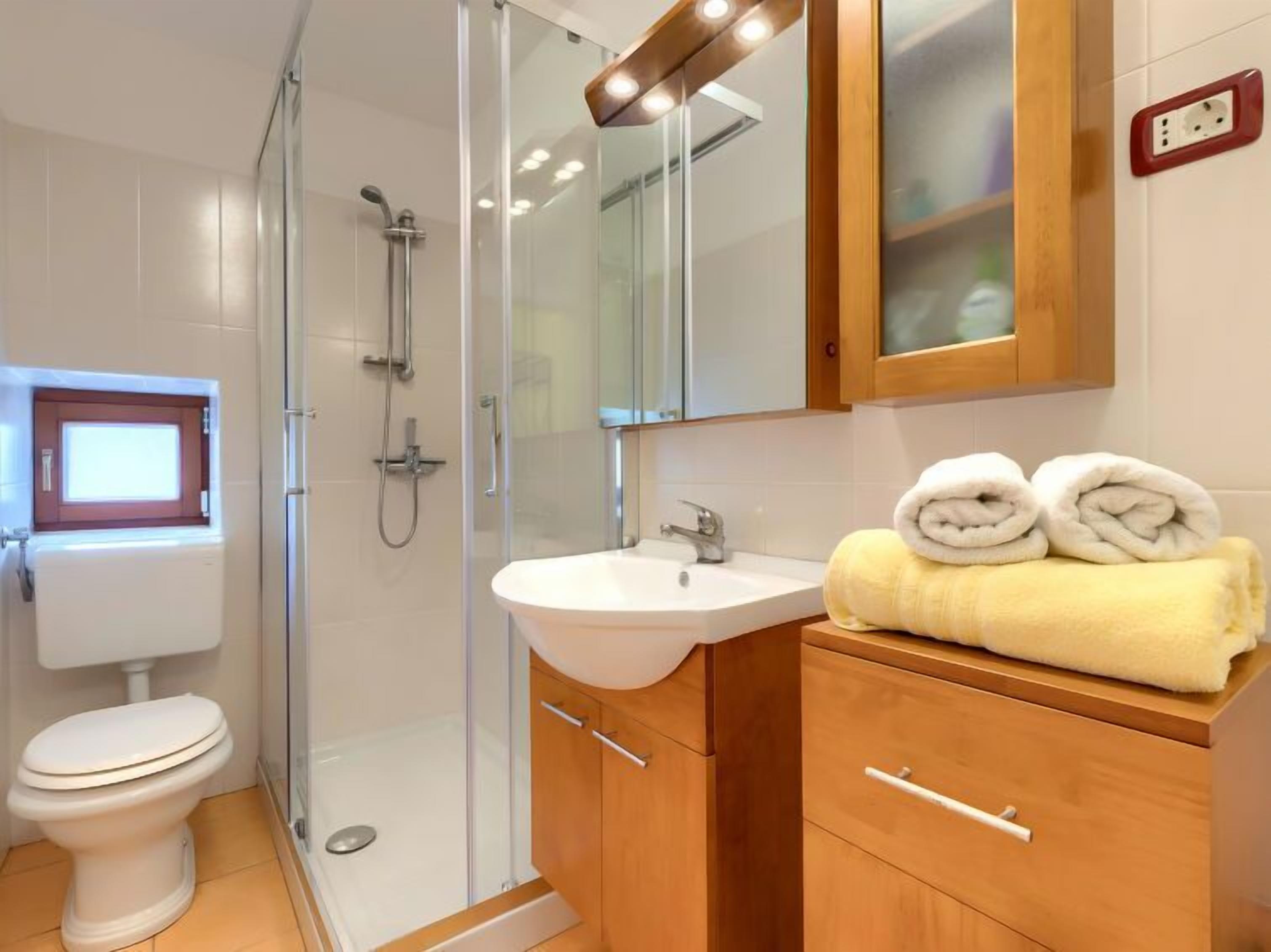 Une salle de bain moderne avec une douche à parois de verre, un lavabo blanc, des meubles en bois et un miroir au-dessus du lavabo.
