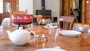 A wooden interior with a dining table set for two, a red decorative bowl, a white teapot, and a fireplace. - Vacation home Dufaux by Interhome (Champex)