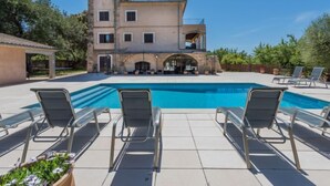 A pool with lounge chairs, a stone building with multiple windows and balconies, and a clear blue sky. - Les Mines by Interhome (Selva)
