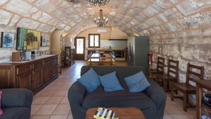 A cozy living room with a stone ceiling, a sofa with blue cushions, a wooden coffee table, and a kitchen in the background. - Les Mines by Interhome (Selva)