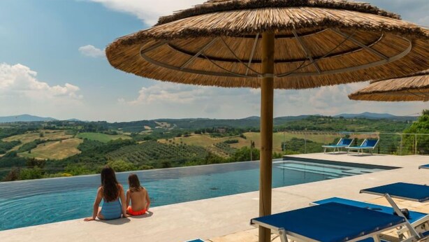 Ein Pool ohne Ende mit Blick auf sanfte Hügel, ein Paar sitzt am Pool, und es sind mehrere Liegestühle vorhanden.
