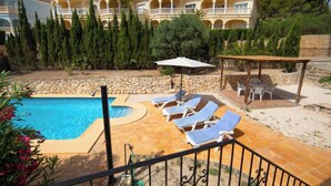 A pool area with lounge chairs, a pergola, and a stone wall.