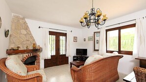 A living room with wicker furniture, a stone fireplace, a television, and a chandelier.
