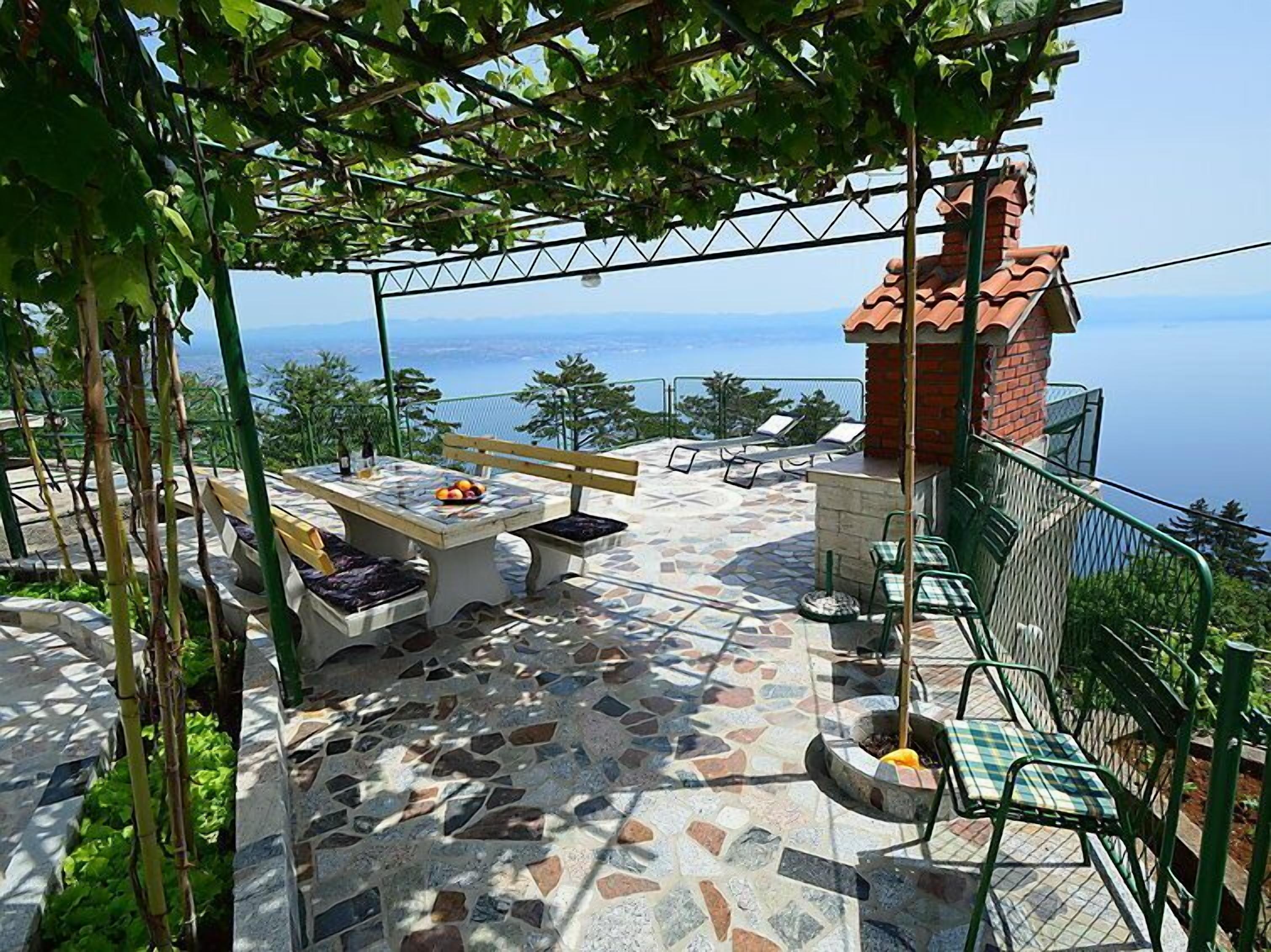 Une terrasse extérieure avec un sol en pierre, une table garnie de fruits et une vue sur la mer.