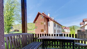A wooden bench and table set on a paved patio with a view of a building with a red roof and white walls. - Nad Łomniczką by Interhome (Karpacz)