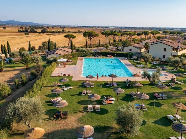 A large rectangular swimming pool surrounded by lounge chairs and umbrellas, with a view of a rural landscape in the background.