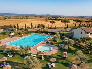 A large rectangular pool with a circular hot tub, surrounded by a grassy area with lounge chairs and umbrellas.