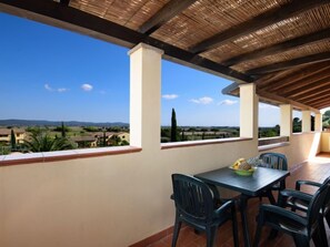 A covered outdoor dining area with a table and chairs, large windows offering a view of the countryside.