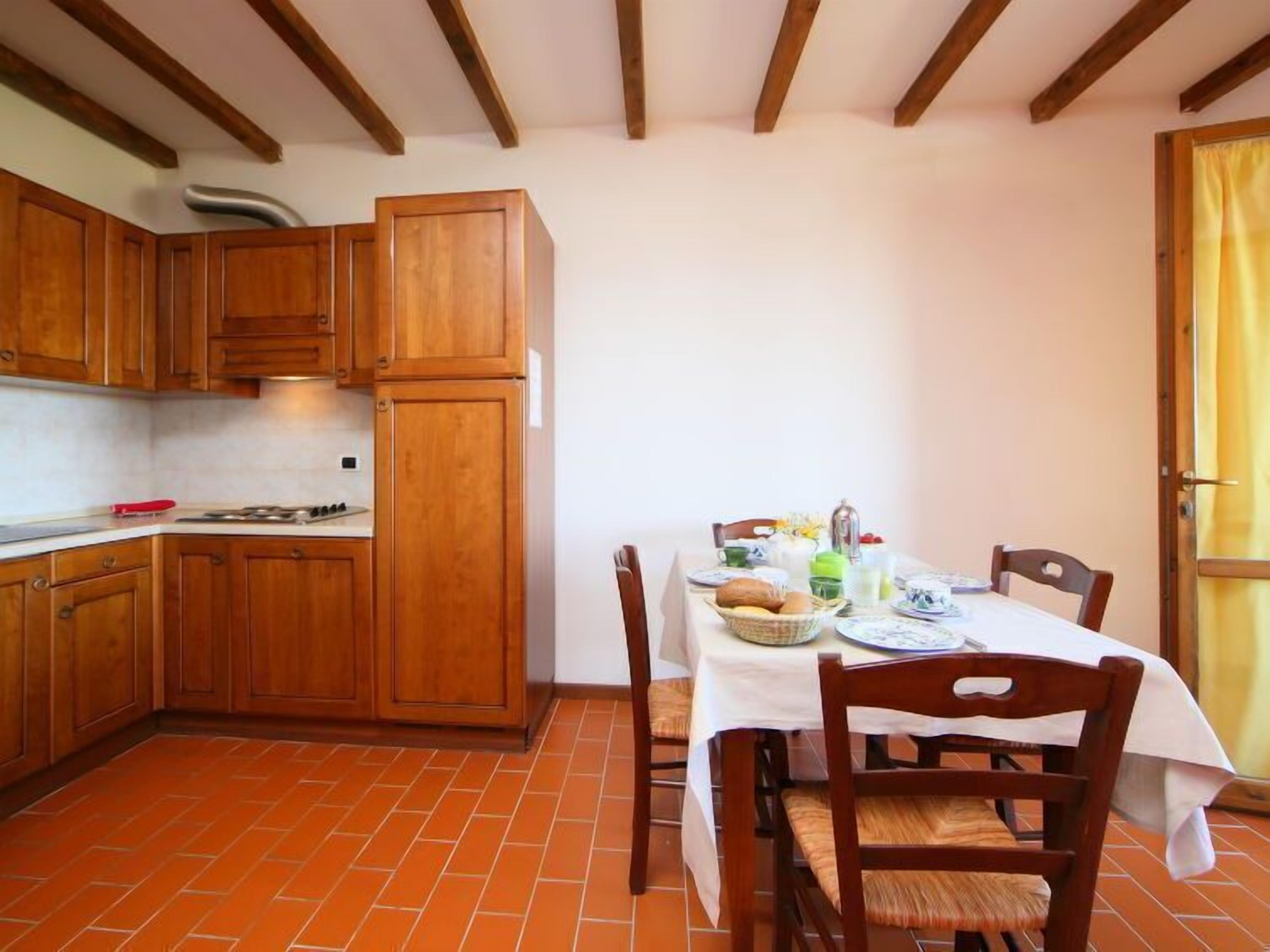 Une cuisine avec des meubles en bois, une table à manger dressée avec de l’assiette et un sol carrelé.