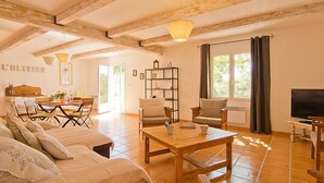 Ein geräumiges Wohnzimmer mit Holzboden, einem Essbereich mit Tisch und Stühlen, einer Couch, einem Bücherregal und einem Fernseher.