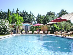 A swimming pool with lounge chairs and umbrellas, surrounded by trees and a building with a tiled roof. - L'Olivier by Interhome (L'isle sur la Sorgue)